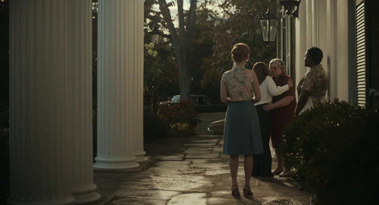 Priscilla (2023) movie still: fullbody — A stone porch features white classical columns and hanging lanterns during the day. Four women gather near…