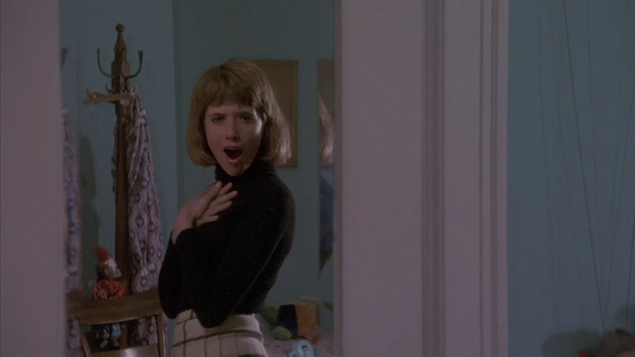 Baby It’s You (1983) movie still: medium — A light blue room with a mirror and a wooden clothes stand in view. The woman stands before the…