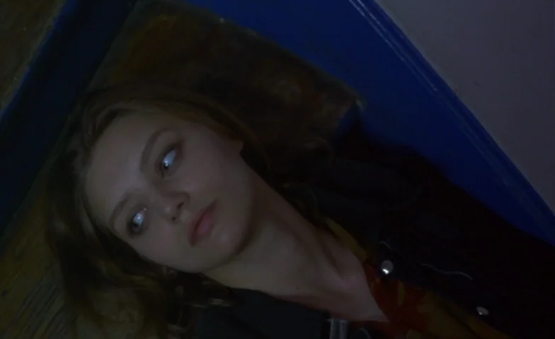 I Can’t Sleep (1994) movie still: closeup — A dimly lit narrow space with blue painted walls and wooden flooring. A young woman lies on the floor…
