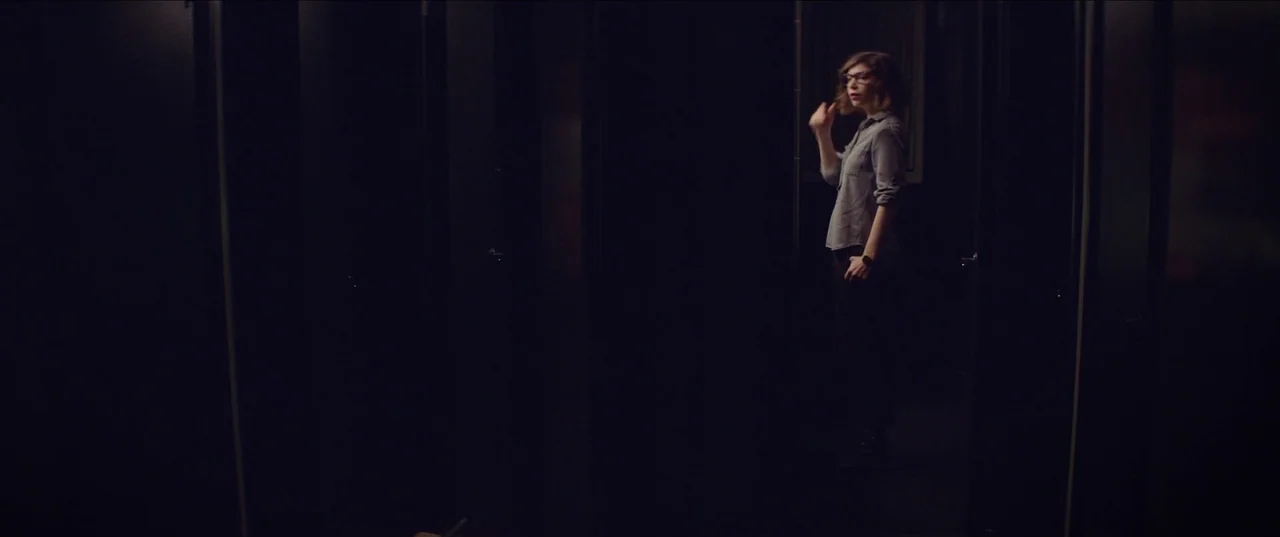 The Nowhere Inn (2020) movie still: wide — A dark, narrow corridor features vertical paneling and deep shadows across the walls. A young woman…