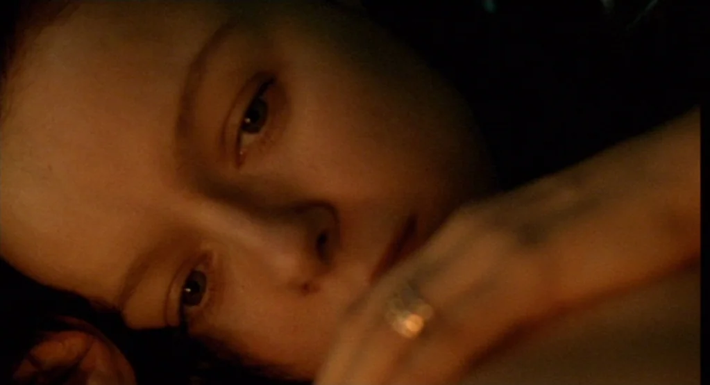 Morvern Callar (2002) movie still: closeup — A close view of a face resting against a surface in low light. A hand with a metallic ring is…