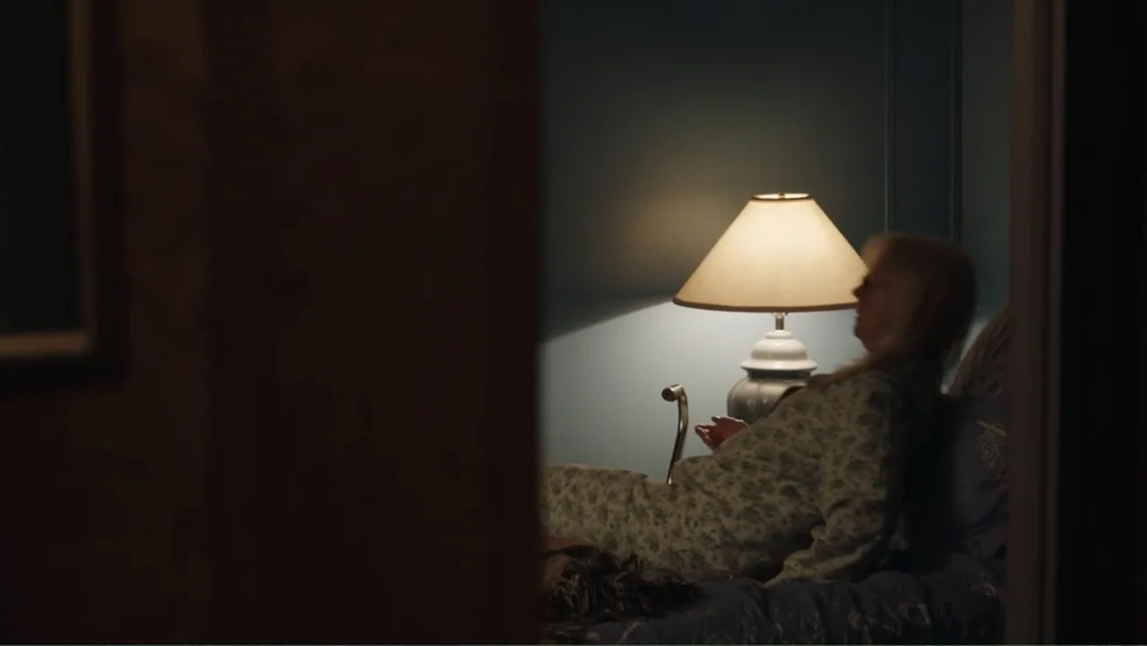 The Cleaner (2021) movie still: medium — A dimly lit room features a woman sitting up in a bed at night. A bedside lamp casts a warm glow against…