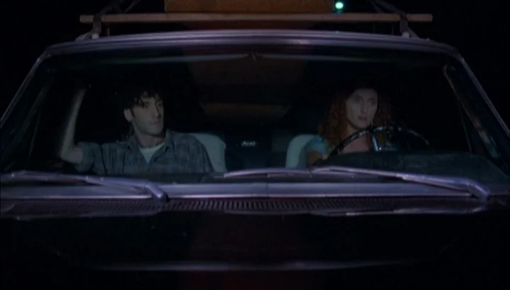 Highway 61 (1991) movie still: medium — The interior of a car at night seen from the front windshield perspective. A man and a woman sit side by…