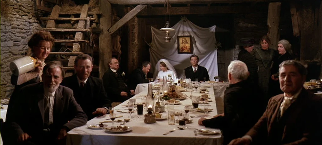 Ryan’s Daughter (1970) movie still: wide — A rustic barn interior converted into a formal banquet hall for a wedding meal. Numerous guests sit…