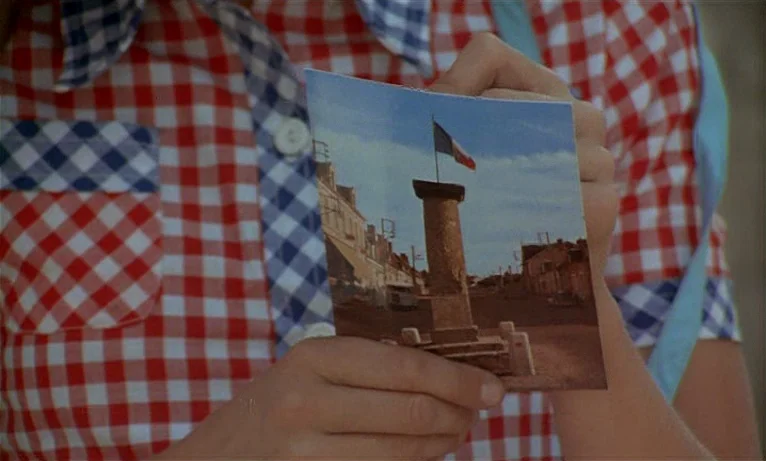 Small Change (1976) movie still: closeup — A person wears a red and white gingham shirt while holding a small color photograph. The photograph…