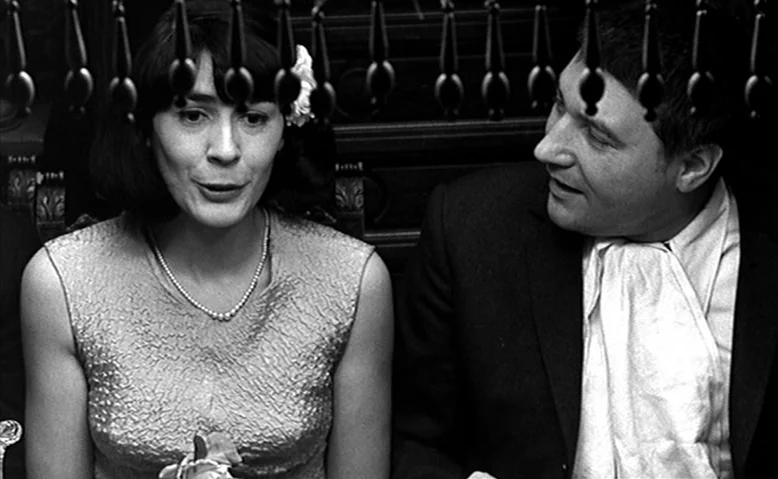 Who Are You, Polly Maggoo? (1966) movie still: medium — A woman and man are seated next to each other in a dimly lit space. Decorative wooden beads…