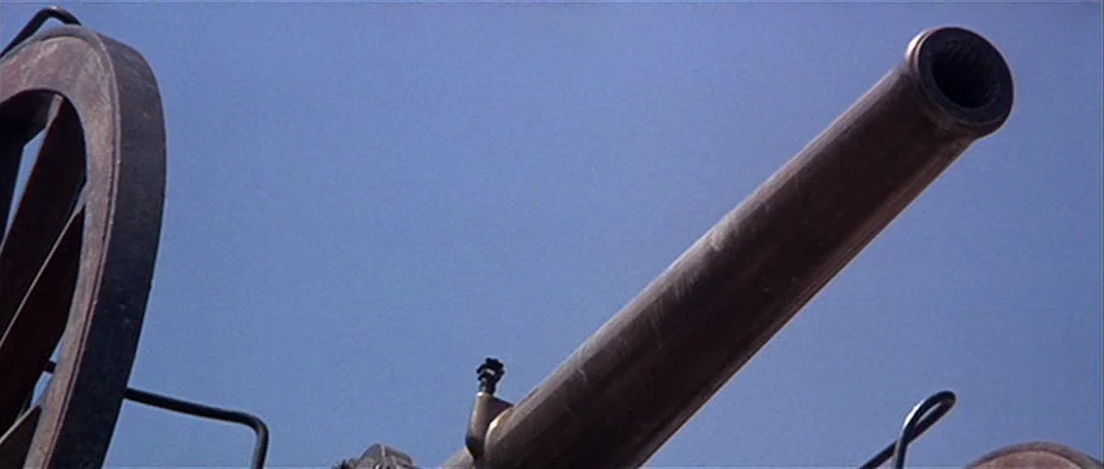 The Good, The Bad And The Ugly (1966) movie still: closeup — A close-up view of a metal artillery cannon pointed upward against a clear sky. The…
