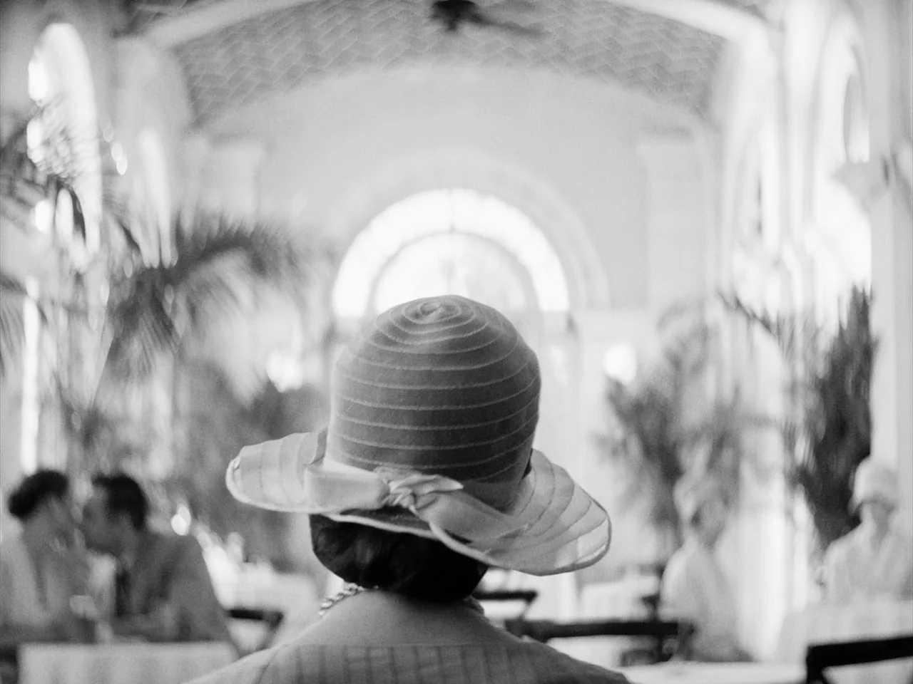 Passing (2021) movie still: closeup — A sunlit room features arched ceilings and decorative potted plants in the background. A woman wearing a…