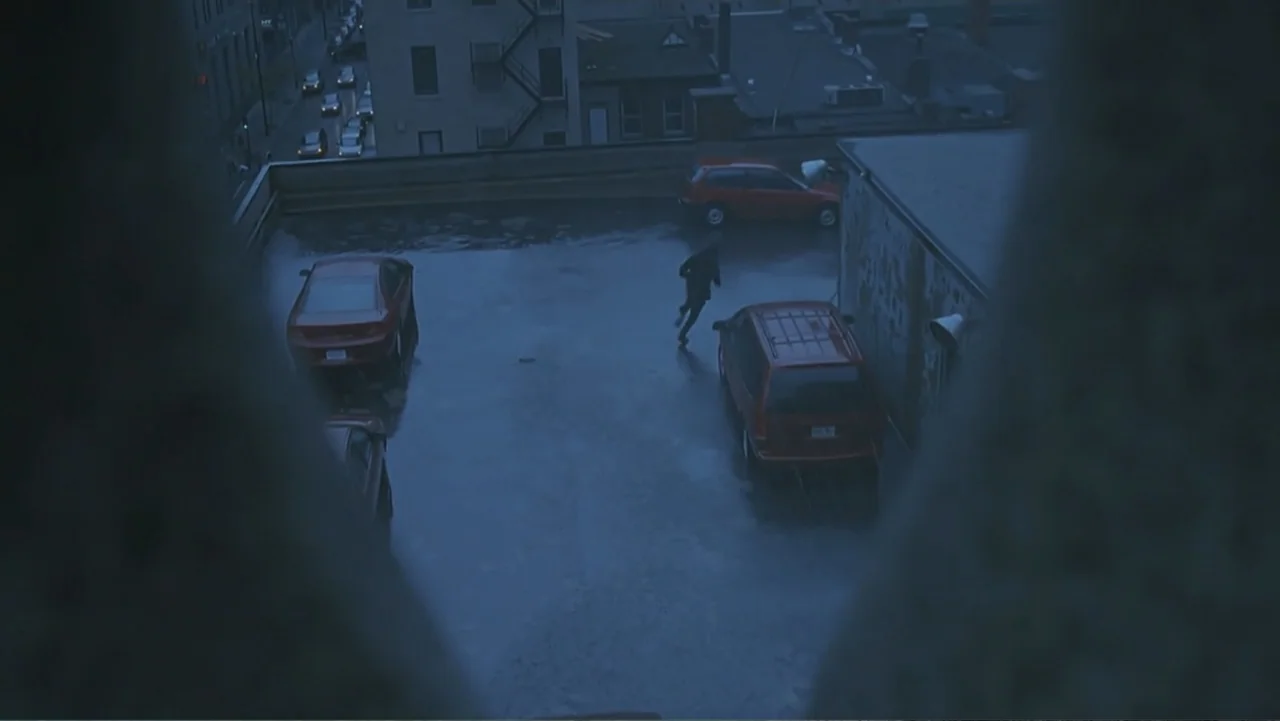 The Art of War (2000) movie still: wide — A dark urban parking lot at night features wet pavement and several parked vehicles. A lone person in dark…