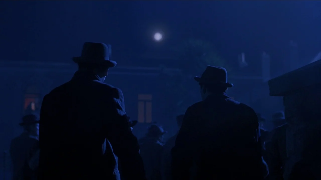 Michael Collins (1996) movie still: medium — A group of men in overcoats and hats walk through a dark town square. The full moon hangs high in the…