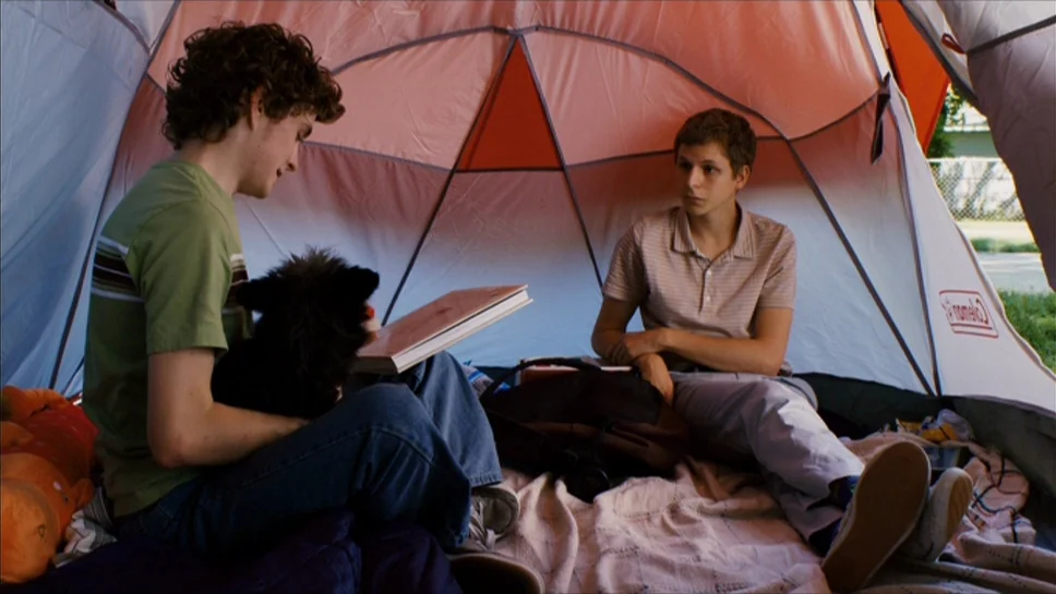 Youth In Revolt (2009) movie still: medium — Two teenage boys sit inside a small red and white nylon tent. They hold a book and sit on a blanket…