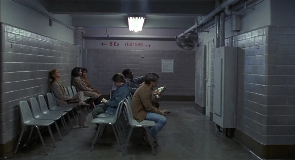 Light Sleeper (1992) movie still: wide — A long windowless hospital waiting area features institutional gray tiled walls and metal chairs. Several…