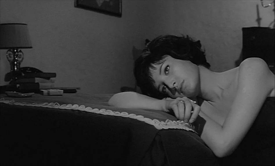 La Notte (1961) movie still: medium — A dimly lit room features a woman lying on a bed. She rests her head on her arms while looking ahead.