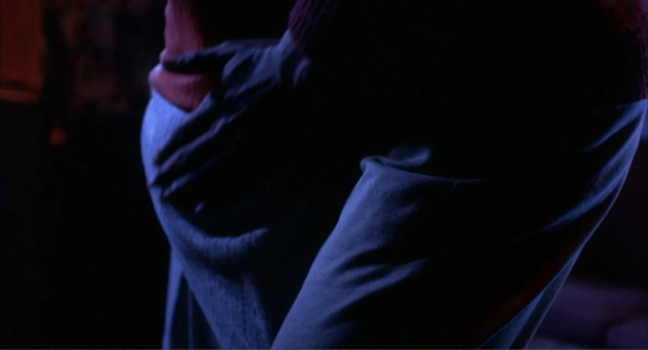 Cooley High (1975) movie still: closeup — A dark interior space features a person's hip and a resting hand in low light. The hand is positioned on…