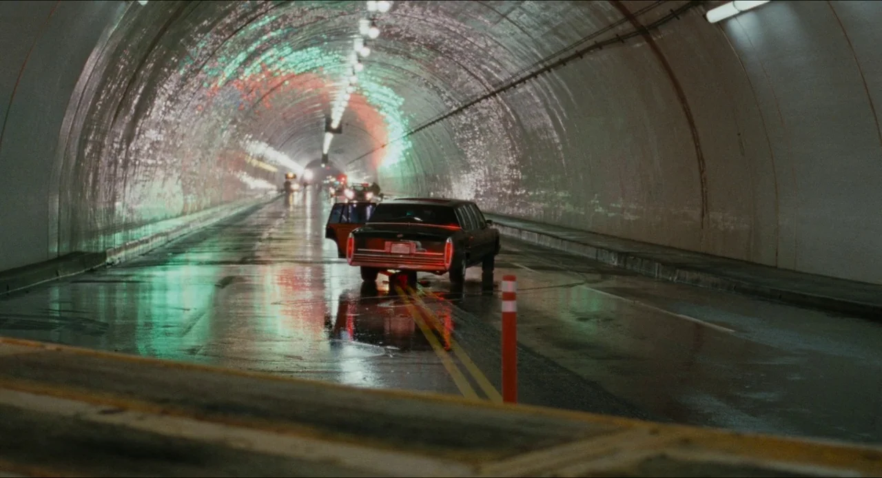 Deep Cover (1992) movie still: wide — A long, curved concrete road tunnel shows wet surfaces reflecting neon light. A dark limousine is parked in…