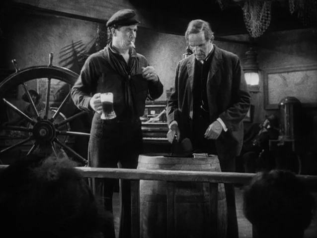 The Docks of New York (1928) movie still: medium — A dark, wood-paneled maritime establishment features a large ships wheel and hanging netting. A…