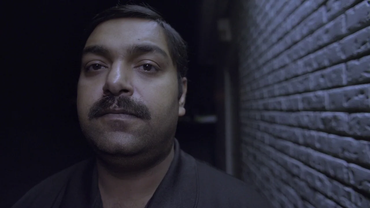 Florida Man (2015) movie still: closeup — A dark urban alleyway features a prominent brick wall in the background. A man stands in the foreground,…