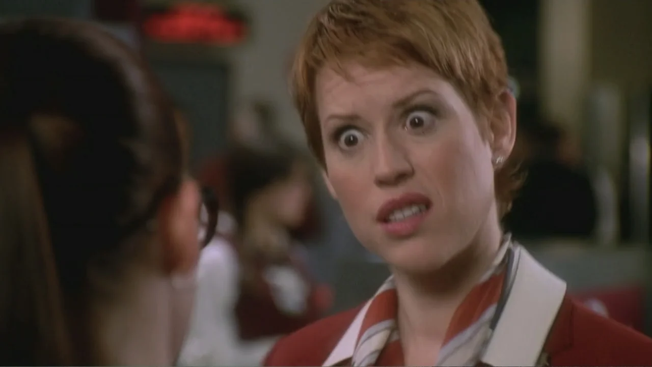Not Another Teen Movie (2001) movie still: closeup — A brightly lit interior of a diner with blurred figures in the background. A woman in a red…