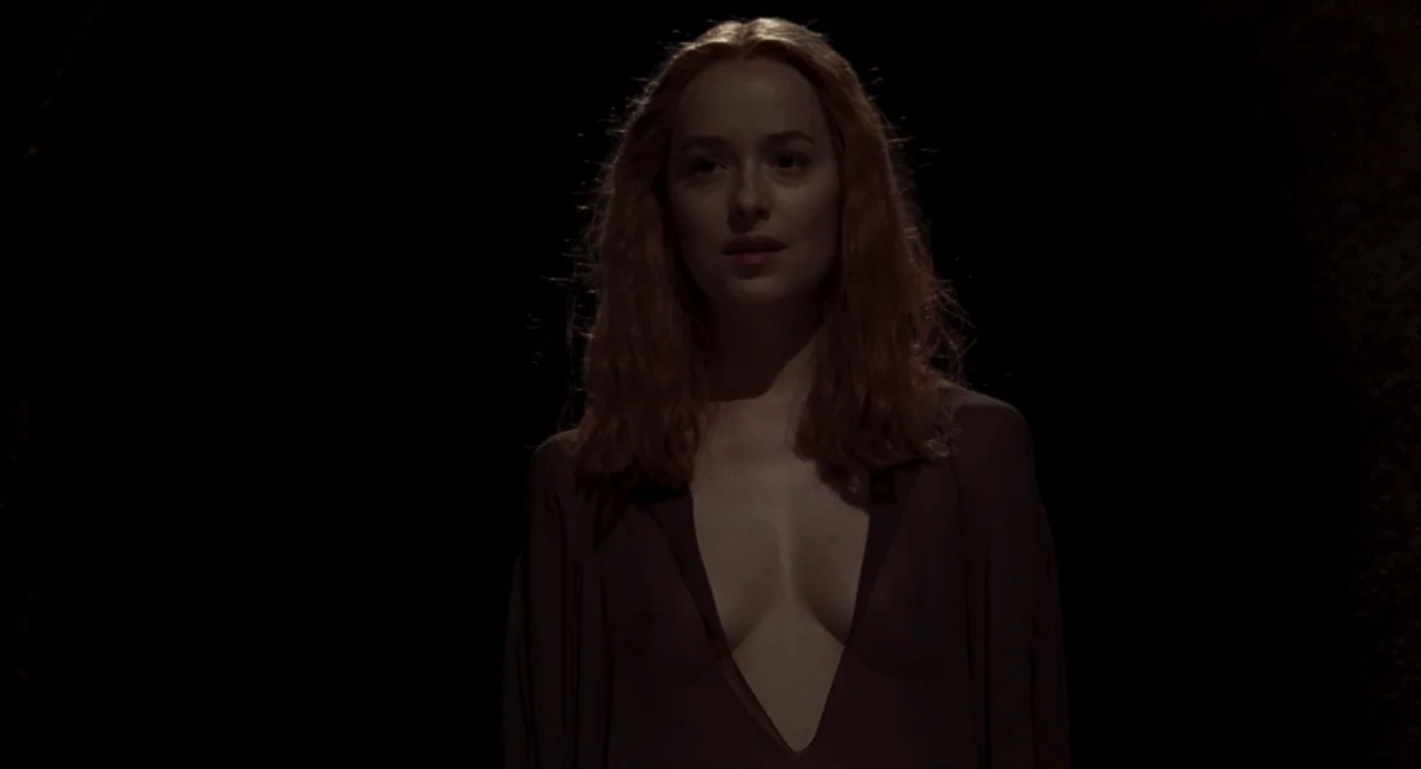 Suspiria (2018) movie still: medium — A woman stands in a completely dark environment with no visible architectural features. She faces the camera…