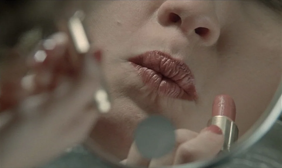 Mr. Klein (1976) movie still: closeup — A close reflection of a woman's lower face appears in a small circular mirror. She holds a lipstick tube and…