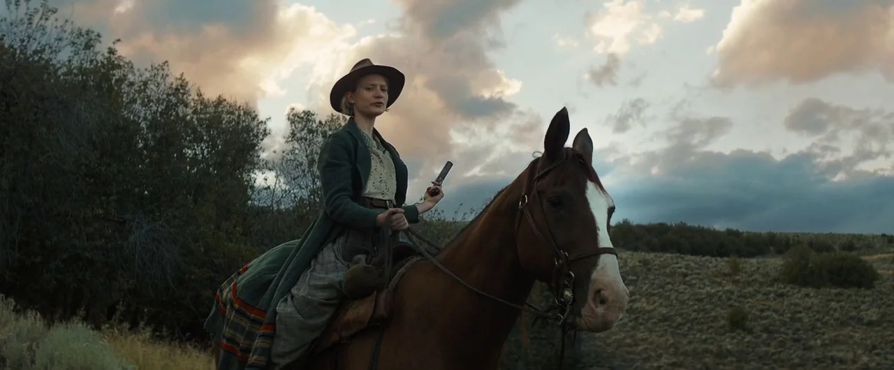 Damsel (2018) movie still: medium — A rider on a brown horse travels through an expansive prairie landscape at dusk. The woman holds a pistol in her…