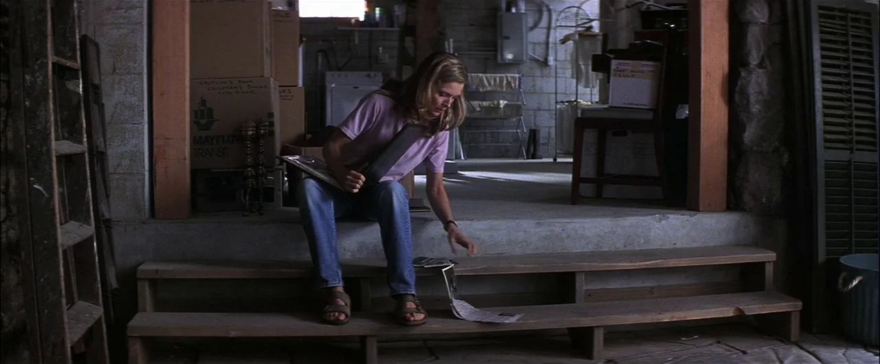 What Lies Beneath (2000) movie still: fullbody — A cluttered basement contains cardboard storage boxes, a laundry rack, and wooden stairs. A young…