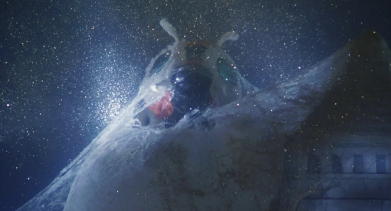 Godzilla and Mothra: The Battle for Earth (1992) movie still: closeup — A giant insect-like creature with compound eyes pushes through a layer of…