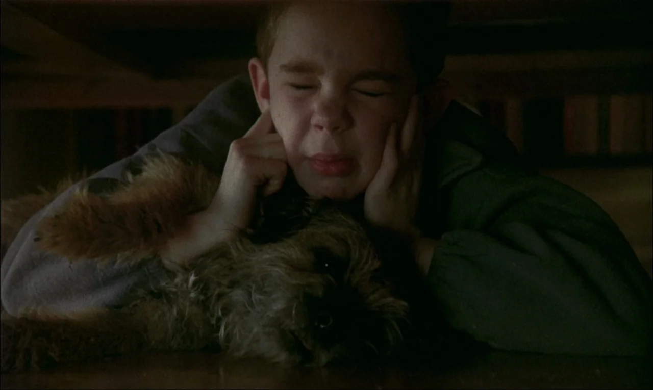 My Life As A Dog (1985) movie still: closeup — A dark, cramped space underneath a piece of wooden furniture like a dining table. A young boy lies…