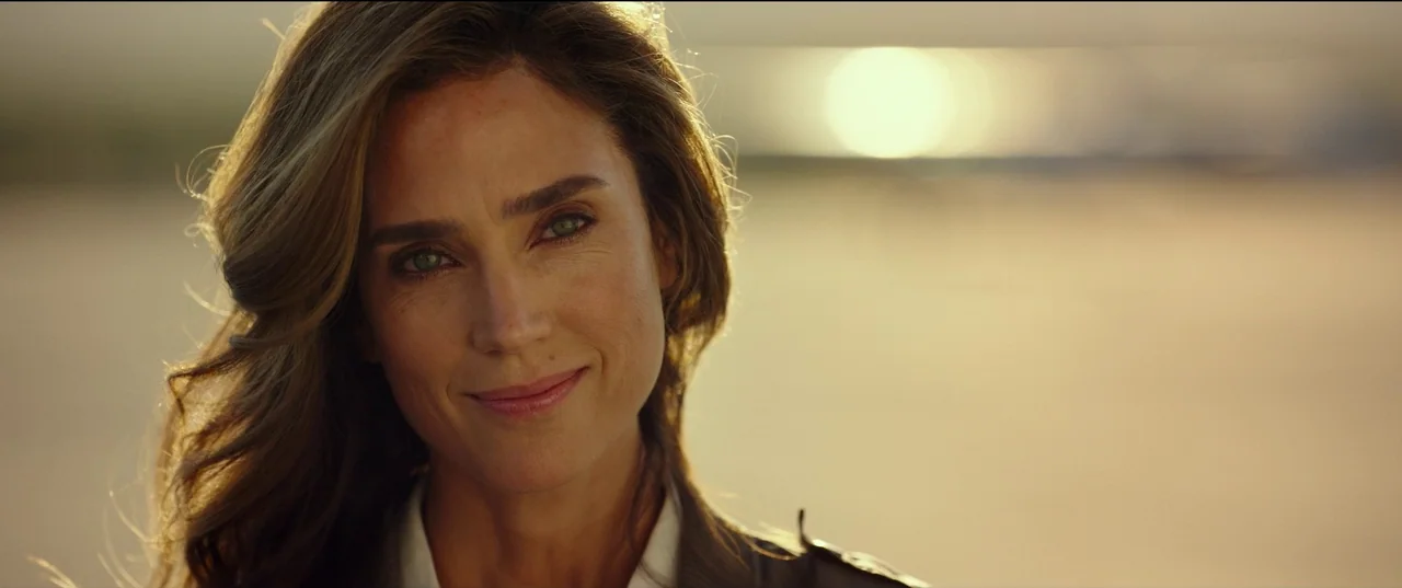 Top Gun: Maverick (2022) movie still: closeup — A woman stands in an open, golden-lit outdoor space. She faces the camera while the background is…