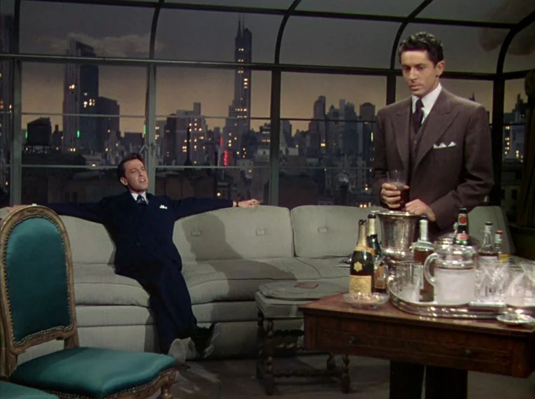 Rope (1948) movie still: medium — A high-rise apartment overlooks a city skyline through a large grid-patterned window at night. One man rests on a…