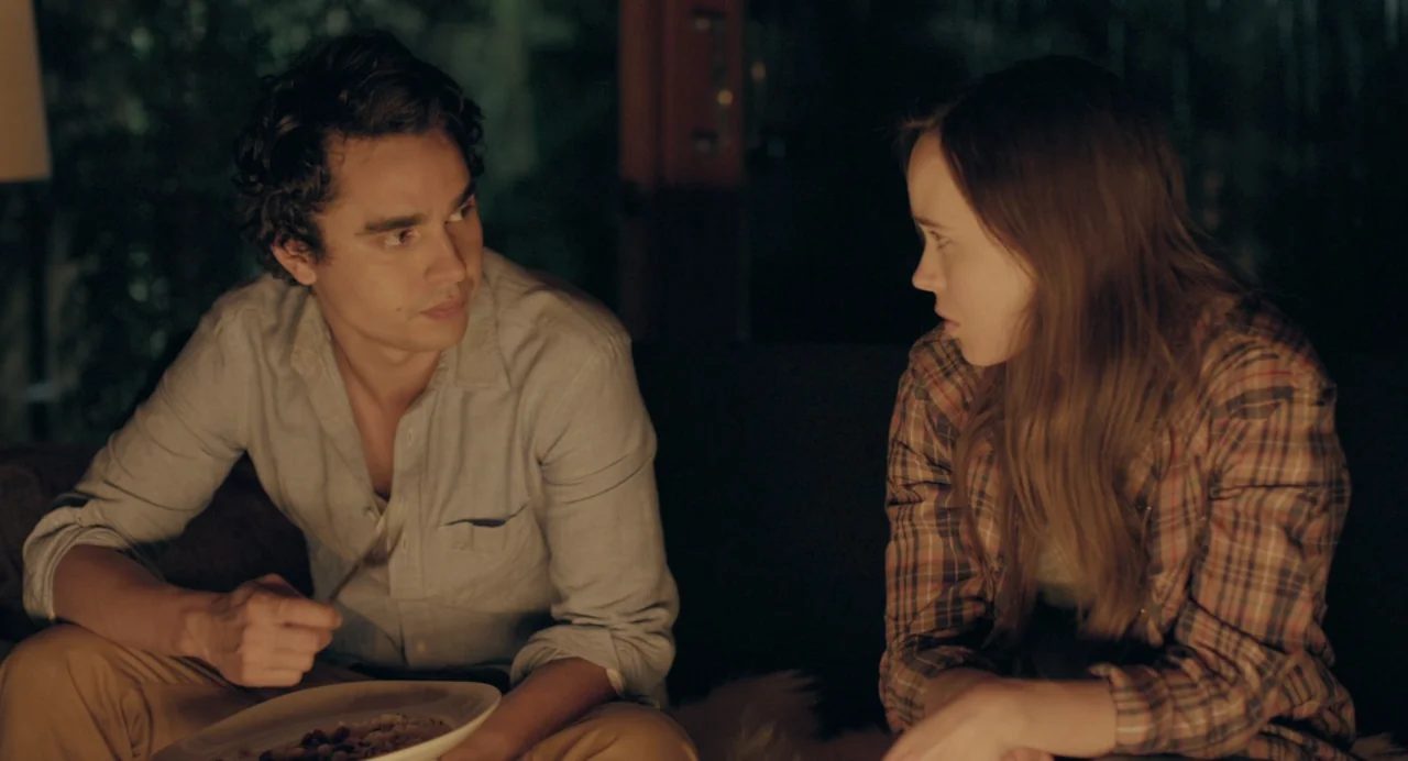 En lo profundo del bosque movie still: medium — A dimly lit indoor space with blurred vegetation visible through a dark glass wall. A young man and…
