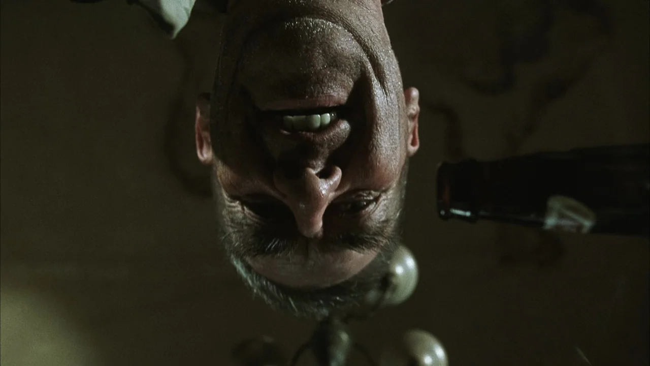 The Texas Chainsaw Massacre (2003) movie still: closeup — An interior space is dimly lit with overhead light fixtures visible in the background. A…