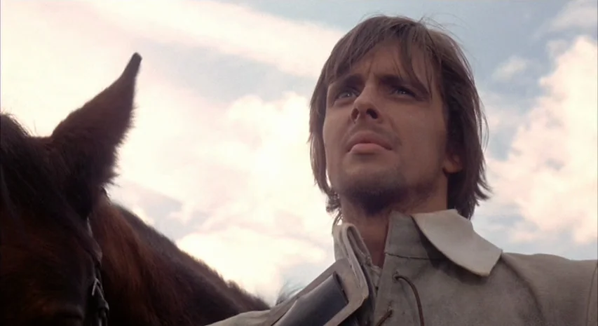 Witchfinder General (1968) movie still: medium — An open landscape with a clear sky serves as the background. A young man with brown hair stands…