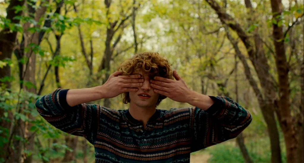 Heartbeats (Les Amours Imaginaires) (2010) movie still: medium — A man stands in a dense woodland clearing with trees and foliage in the background.…
