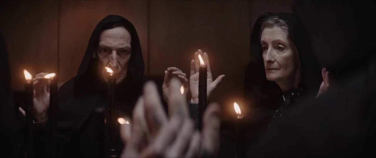Anything For Jackson (2020) movie still: medium — A dimly lit room with multiple figures dressed in dark hooded robes surrounding a table. The…
