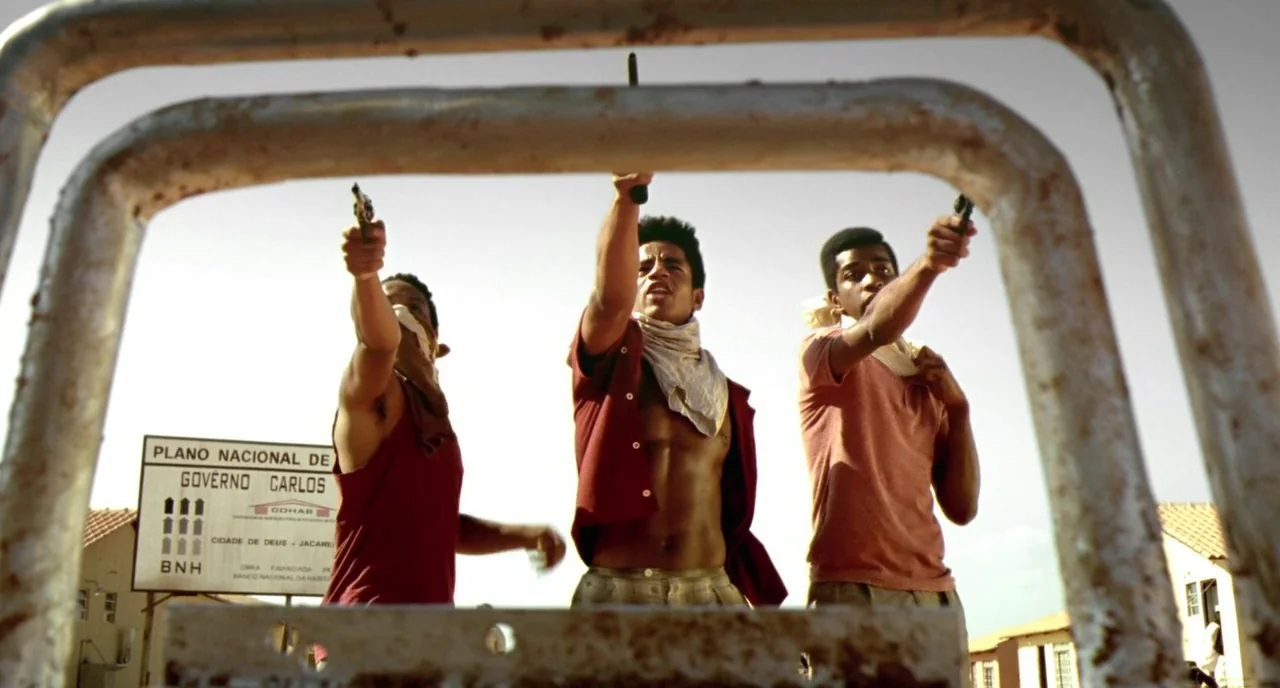 City of God (2002) movie still: medium — A low-angle view of three young men standing in a residential housing project. The trio holds firearms…