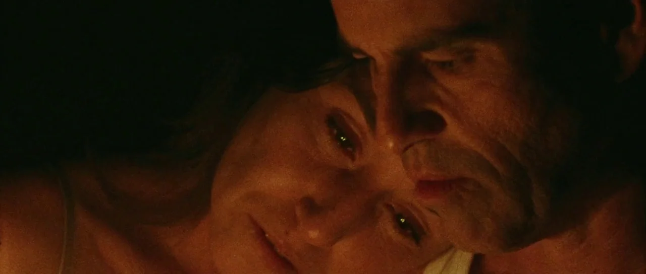 Alléluia (2014) movie still: closeup — Two individuals lie close together in a dark room. Their faces are illuminated by a warm, low-level light…