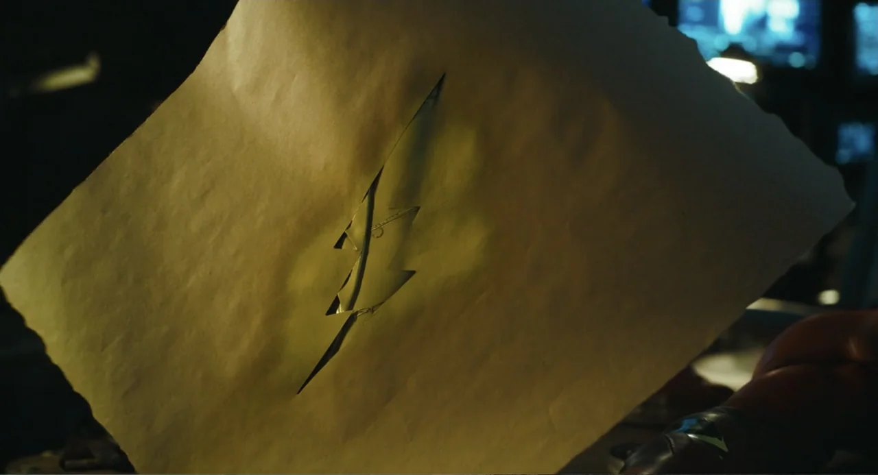 The Flash (2023) movie still: closeup — A piece of textured, tan paper features a sharp, lightning-bolt-shaped cutout in its center. The paper is…
