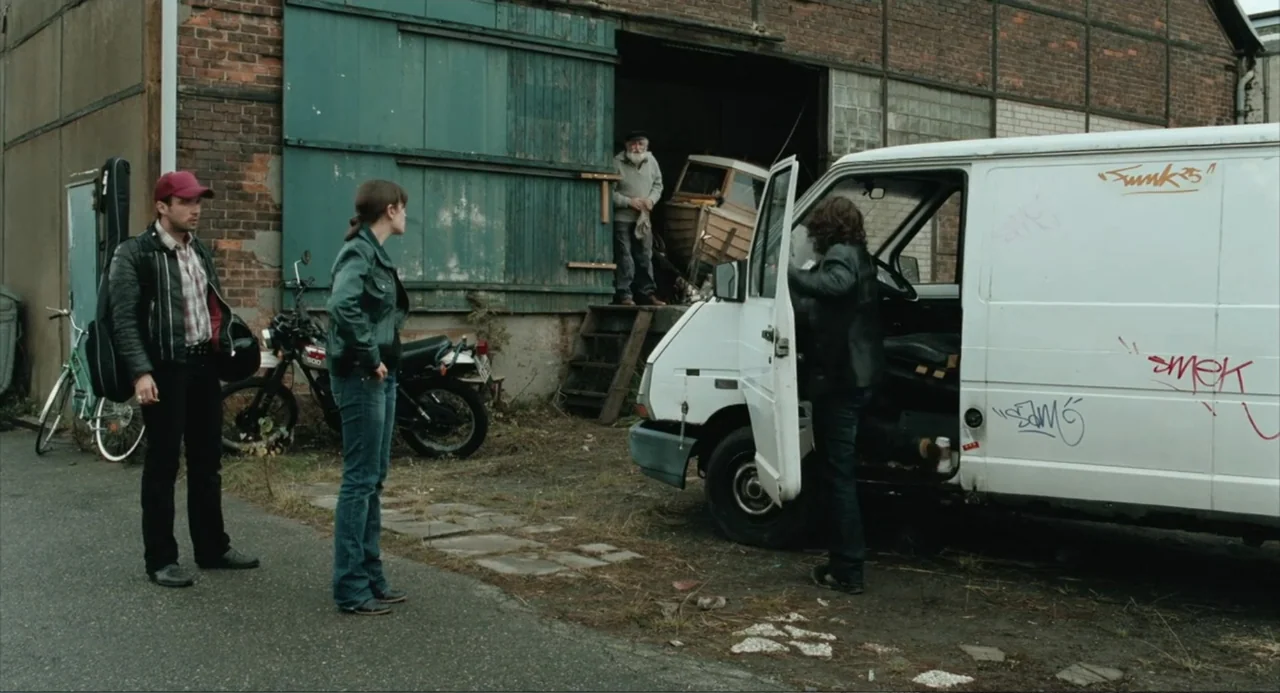 Soul Kitchen (2009) movie still: fullbody — A gravel-surfaced yard features a weathered brick building with large sliding wooden doors. Three…