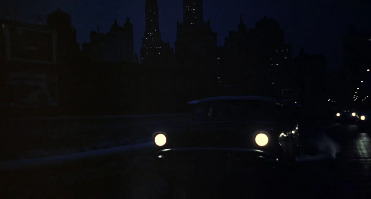 Bell Book and Candle (1958) movie still: wide — A dark night highway stretches before a silhouetted skyline of early twentieth-century buildings. A…
