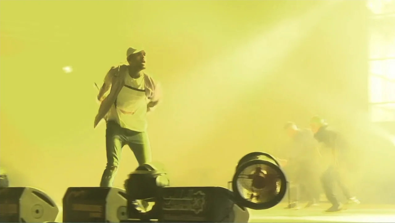 Chris Brown: A History of Violence (2024) movie still: fullbody — A brightly lit performance stage is filled with thick yellow haze and stage…