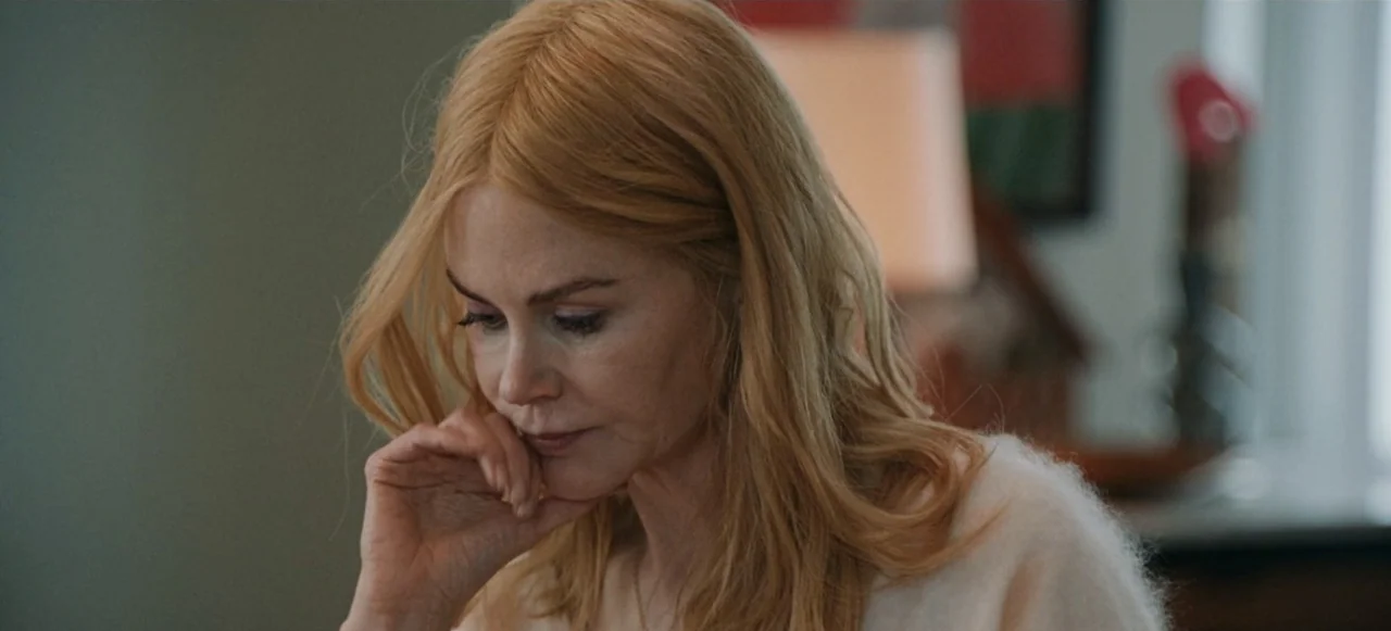 Babygirl (2024) movie still: closeup — A bright domestic interior with neutral walls and a blurred lamp in the background. A woman in a soft knit…