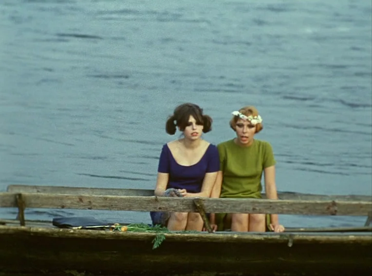 Daisies (1966) movie still: medium — Two young women sit on a weathered wooden boat floating on a river. They remain seated together while the boat…