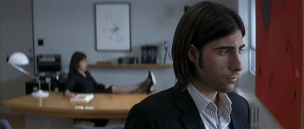 I Heart Huckabees (2004) movie still: medium — A contemporary professional workspace featuring a curved wooden desk and minimalist wall art. A man…