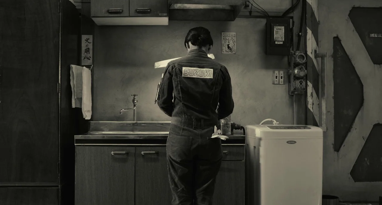 The Whispering Star (2015) movie still: medium — A utilitarian room features a basic metal sink, cabinets, and a white washing machine. A person in…