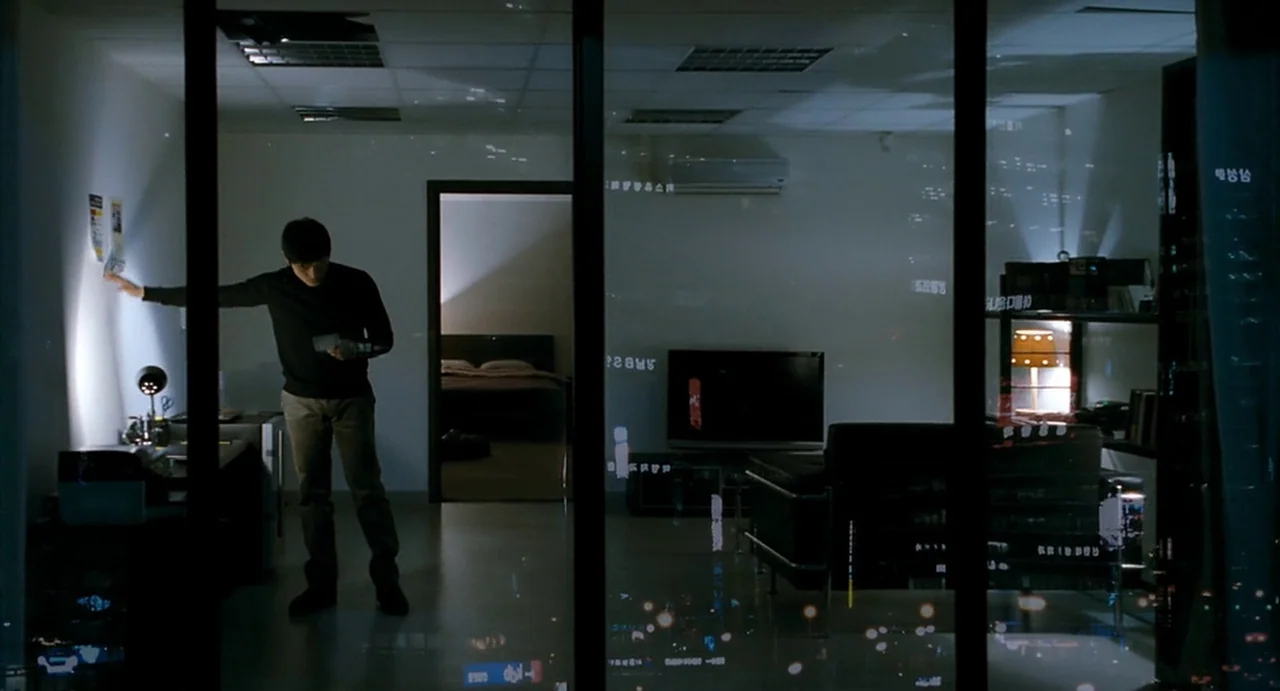I Saw The Devil (2010) movie still: wide — A minimalist modern apartment interior with dark furniture and large glass window partitions. A man…