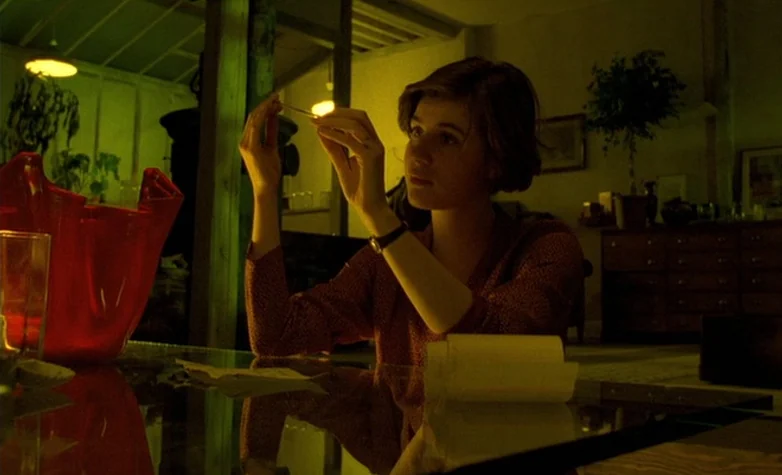 The Double Life of Véronique (1991) movie still: medium — A dimly lit room features a glass table and a large red decorative object. A young woman…