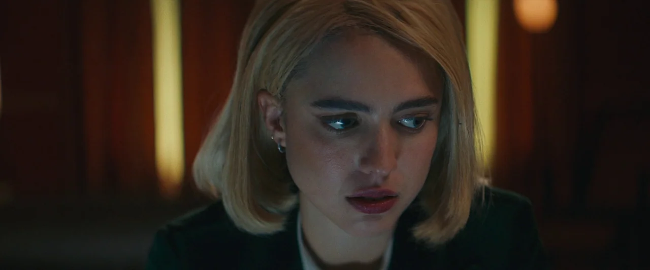 Sanctuary (2023) movie still: closeup — A dimly lit room features a woman centered in the frame against vertical wooden panels. She looks downwards…