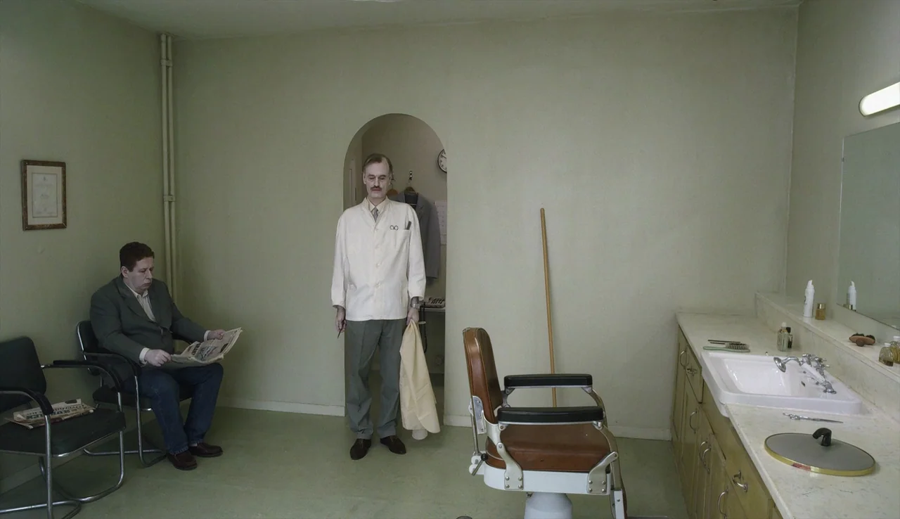 A Pigeon Sat on a Branch Reflecting on Existence (2014) movie still: wide — A spartan room features beige walls, a brown leather chair, and a white…