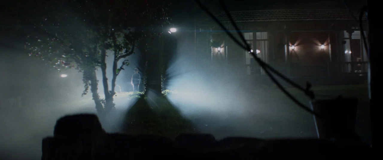 Colour Out of Space (2020) movie still: wide — A night exterior shows a dark yard filled with dense, low-hanging fog. A small figure stands alone on…